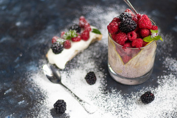 Chia seeds soaked in yogurt are sprinkled on the bottom of the glass, then cookies are placed, and raspberries are on top. Behind a glass with pear tincture. Everything stands on a dark background. 