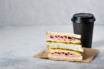 Ham and cheese sandwich and paper cup with coffee. The concept of fast food and coffee to go. Light background. Close-up. Free space for text.