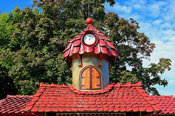 tiled roof with a clock tower on the background of green foliage and blue sky