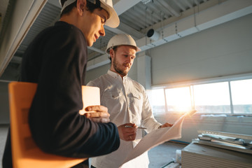 Building industry. Young engineer discussing with building worker on construction site. Industrial...