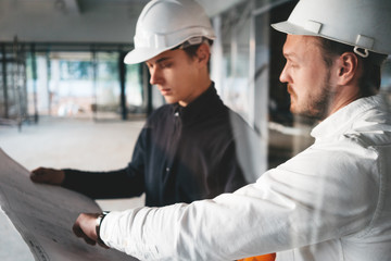Industrial architect discussing build drawing with worker wearing safety hard hat. Two building engineers lookin at blueprint on construction site