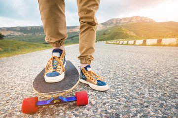 Close-up of male legs in rag sneakers on a longboard on the background of asphalt at sunset. Big skateboard with man legs. Youth leisure concept