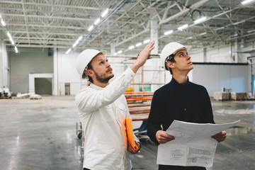 Building engineer and worker hold blueprint in hand while discussong construction site. Industrial engineers have meeting on build