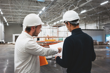 Building industry. Young engineer discussing with building worker on construction site. Industrial engineers have meeting while uses blueprint