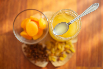Spoon on a glass jar with honey, dried apricots and raisins on a wooden table.