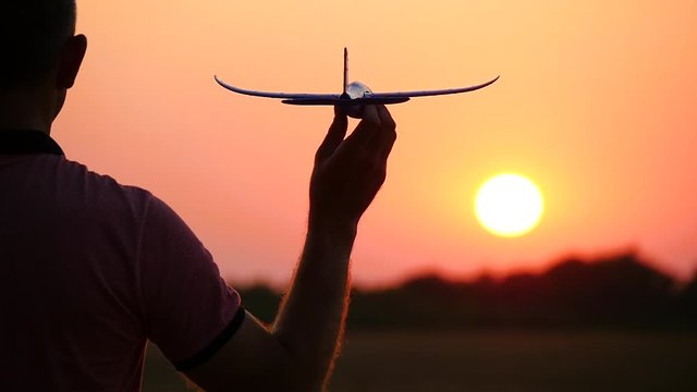 Silhouette of a men holding in hand a model airplane, standing in front of the sun at sunset. The concept of tourism, air travel.