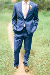 close up of groom's blue suit jacket and pants, modern wedding style, feather boutonniere, pink tie