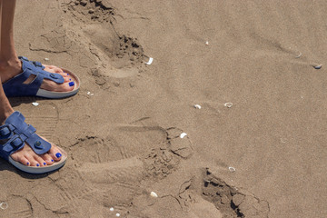 Woman feet with blue painted nails and sandals on the sand