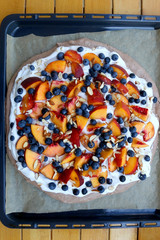 Chocolate Pavlova cake with whipped cream, peaches, blueberries and almonds. Top view.