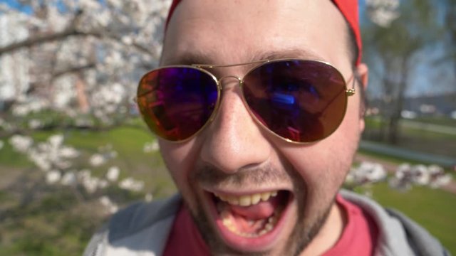 Unshaven crafty man in sunglasses looks at the camera and spiteful laughs