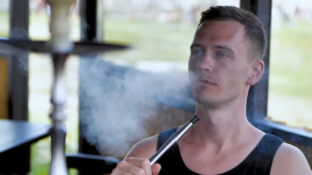 Young man is having fun smoking a hookah in an oriental restaurant at summer day near beach