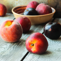 Ripe peaches and plums in a plate on a rustic background