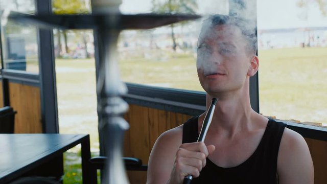 Young man is having fun smoking a hookah in an oriental restaurant at summer day near beach