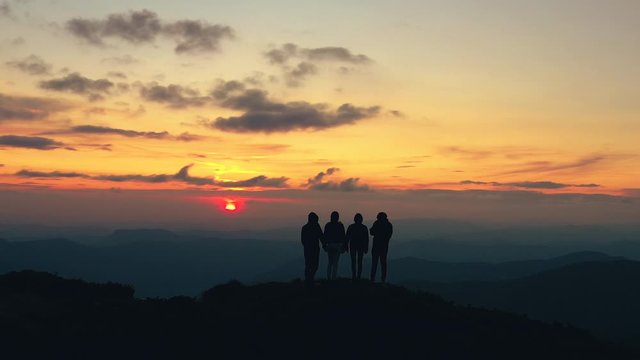 The four people standing on a mountain with the beautiful sunset