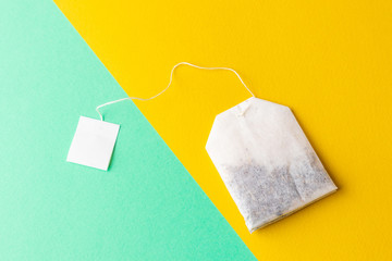 Tea bags with white labels on a pastel green and bright yellow background. Minimalism, flat lay, place for text.