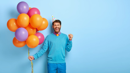 Joyous optimistic man celebrates successful job position, being on corporate party, clenches fist...