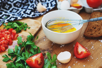 cooking process, ingredients, hearty and healthy breakfast, scramble eggs with tomatoes and herbs on toast with black tea on a wooden background