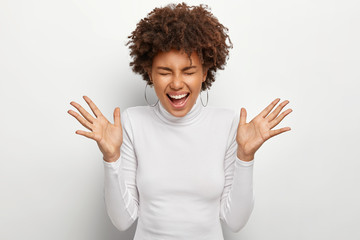 Thrilled joyful woman feels overemotive, laughs out from happiness, shows palms and claps hands,...