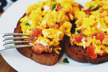 hearty and healthy breakfast, scramble eggs with tomatoes and herbs on toast with black tea on a wooden background