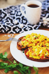 hearty and healthy breakfast, scramble eggs with tomatoes and herbs on toast with black tea on a wooden background