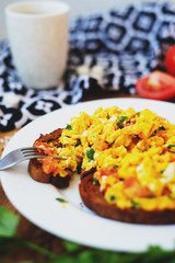 hearty and healthy breakfast, scramble eggs with tomatoes and herbs on toast with black tea on a wooden background
