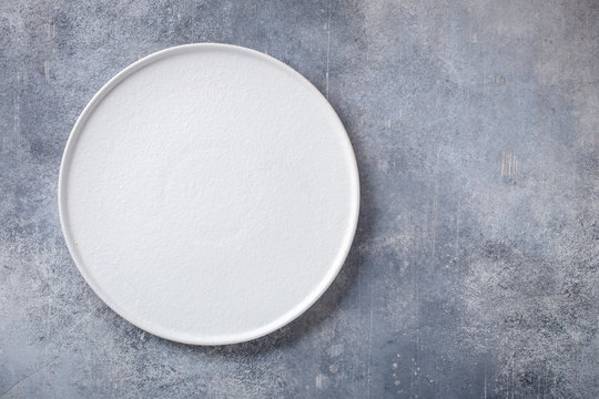 Empty white plate on gray concrete background. Top view, with copy space