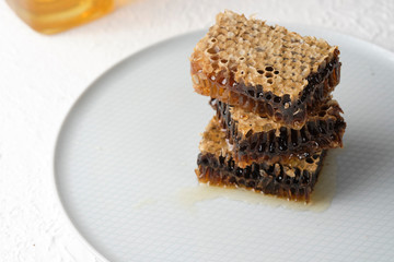 honeycomb with honey lie on a gray plate next to a jar of honey and a honey spoon, selective focus