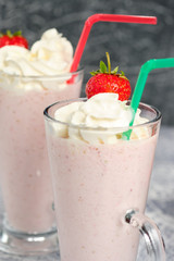 Two glasses with strawberry milkshake with pieces of berries on the edge of the glass on gray background.