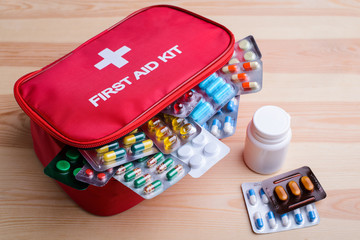 Full-equipped first aid kit with pills and other medicine lays on wooden table. Concept of health...