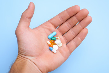 Concept of taking pills. Man`s hand holding different pills capsules against blue background