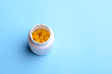 White plastic bottle with yellow ball pills inside. Bottle with prescribed pills stands on the blue table