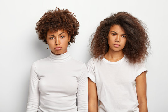 Unhappy bored women with curly hair, have displeased faces, feel embarrassed, being in low spirit, dressed casually in white clothing, have some problem. Negative human facial expressions concept