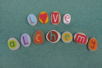 Love Alchemy text composed with creative carved and colored stones over green sand
