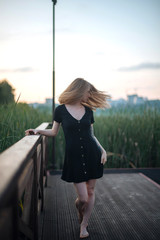 Romantic girl in black dress walking on pier