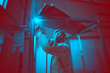 Welder in mask welding metal construction on open air.
