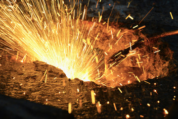 A gas cutter in production, a welder removes unnecessary metal residues with a gas cutter, sparks fly in different directions.