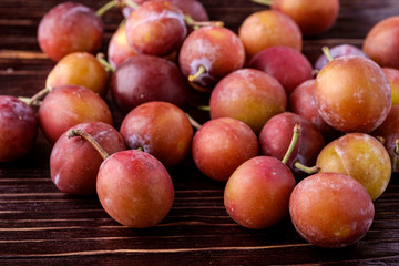 Fototapeta na wymiar Scattered ripe sweet plum fruits on dark moody wood table background, soft light, copy space