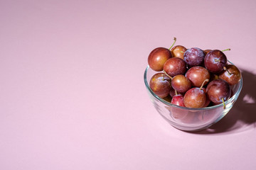 Ripe sweet plum fruits in glass bowl on pink background, hard light, copy space