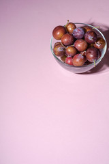 Ripe sweet plum fruits in glass bowl on pink background, hard light, copy space