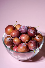 Ripe sweet plum fruits in glass bowl on pink background, hard light, copy space