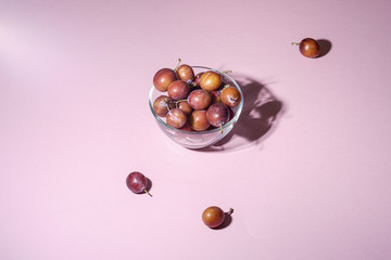 Ripe sweet plum fruits in glass bowl near with scattered plums on pink background, hard light, copy space