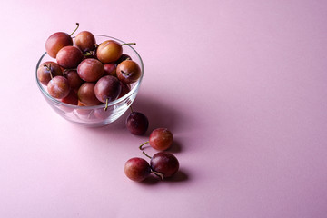Ripe sweet plum fruits in glass bowl near with scattered plums on pink background, soft light, copy space