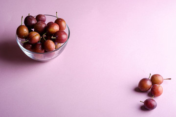 Ripe sweet plum fruits in glass bowl near with scattered plums on pink background, soft light, copy space