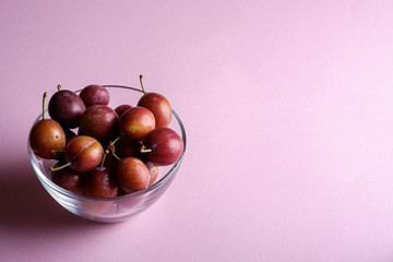 Ripe sweet plum fruits in glass bowl on pink background, soft light, copy space