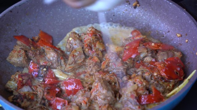 Frying pan with onion, lemongrass, red pepper and beef meat, close up. Indonesia. Sambal Goreng Ati Kentang, Indonesian cuisine, spicy beef meet and potatoes garnish with lemongrass leaf and red chili