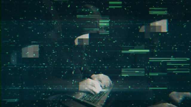 Cyber crime attacks. Man hacker hided face, black sweatshirt and hood is typing on keyboard. Black flashing background interference, striped green lines.