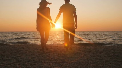 silhouette of a romantic young couple standing on the seashore, man comes up and takes the girl's hand and together enjoying sunrise on the beach, summer vacation and love - Powered by Adobe