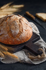 Fresh homemade whole grain bread on a cutting board against a dark background. Selective focus