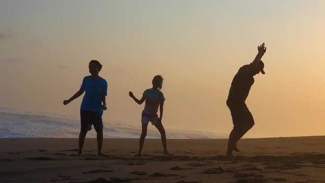 Silhouette of cheerful family dancing on the beach at sunset time while enjoying holiday. Shot in 4k resolution
