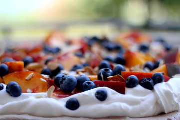 Chocolate Pavlova cake with whipped cream, peaches, blueberries and almonds. Selective focus.